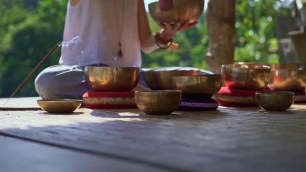 Superslowmotion shot of a woman master of Asian sacred medicine performs Tibetan bowls healing ritual. Meditation with Tibetan singing bowls. She sits in a gazebo for meditation with a beautiful — Stock Video