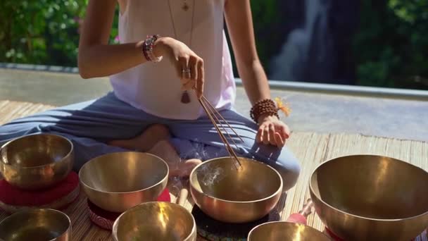 亚洲圣药女大师的超慢动作镜头表演藏碗疗伤仪式。用藏语唱碗冥想。她坐在凉亭冥想与一个美丽的 — 图库视频影像