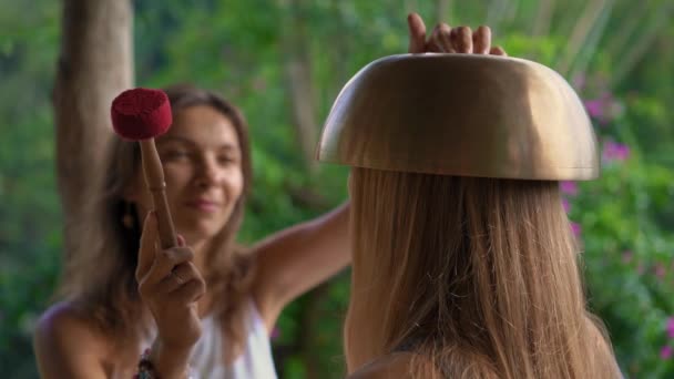 Superslowmotion shot van een vrouw meester van de Aziatische Heilige geneeskunde voert Tibetaanse kommen genezing ritueel voor een cliënt jonge vrouw. Meditatie met Tibetaanse klankschalen. Ze bevinden zich in een prieel voor — Stockvideo