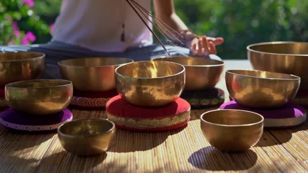 Superslowmotion shot of a woman master of Asian sacred medicine performs Tibetan bowls healing ritual. Meditation with Tibetan singing bowls. She sits in a gazebo for meditation with a beautiful — Stock Video