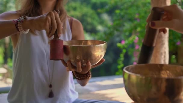 Superslowmotion shot of a woman master of Asian sacred medicine performs Tibetan bowls healing ritual for a client young woman. Meditation with Tibetan singing bowls. They are in a gazebo for — Stock Video