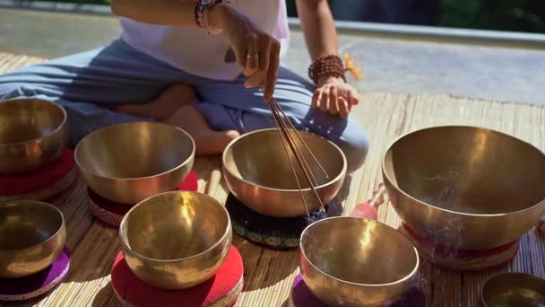 Superslowmotion tiro de uma mulher mestre da medicina sagrada asiática realiza tigelas tibetanas ritual de cura. Meditação com taças de canto tibetano. Ela se senta em um gazebo para meditação com uma bela — Vídeo de Stock