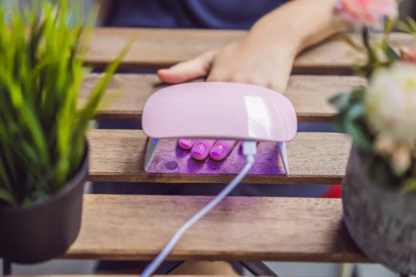 Mulher jovem faz manicure com gel polonês e lâmpada UV em tons rosa — Fotografia de Stock