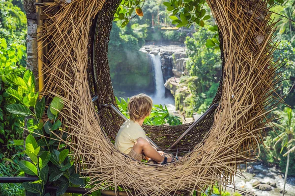 Tendencia Bali, nidos de paja por todas partes. Lugar amigable para niños. Chico turista disfrutando de su viaje por la isla de Bali, Indonesia. Haciendo una parada en una hermosa colina. Foto en un nido de paja, ambiente natural — Foto de Stock