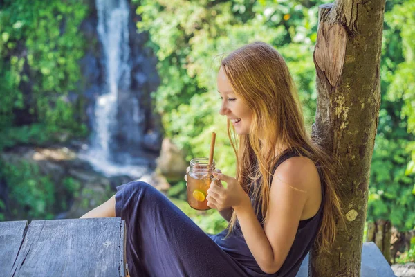 Портретный образ красивой женщины, пьющей чай со льдом с чувством счастья на зеленом фоне природы и водопада — стоковое фото