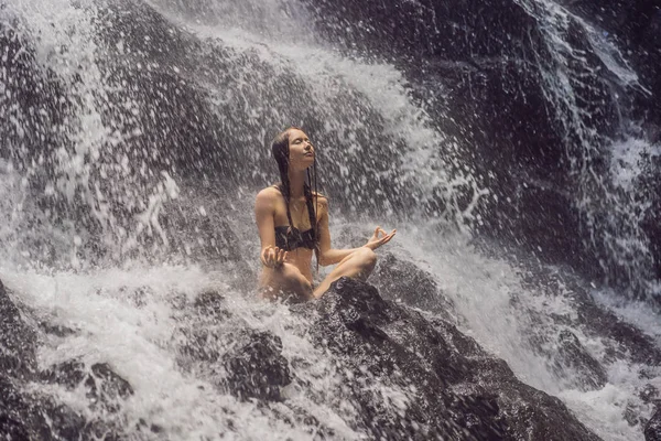 Wellness Spa, vakantie en yoga meditatie concept. Jonge vrouw zittend in lotuspositie op de rots in tropische waterval — Stockfoto