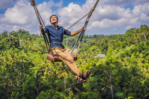 Young man swinging in the jungle rainforest of Bali island, Indonesia. Swing in the tropics. Swings - trend of Bali