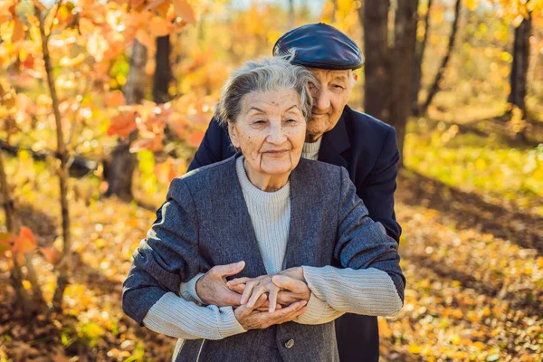 Buoni anziani nella foresta autunnale. famiglia, età, stagione e concetto di persone - felice coppia anziana camminando su sfondo alberi autunnali — Foto Stock