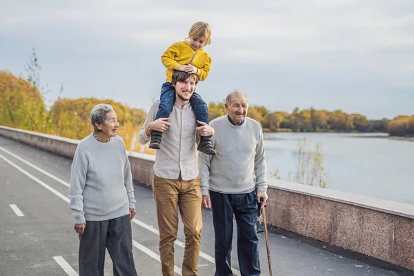 Пожилая пара гуляет по парку с рекой с внуком и правнуком — стоковое фото