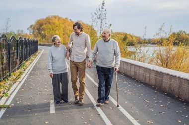 Bir erkek asistan veya yetişkin torunu ile parkta yaşlı bir çift yürür. Gönüllü yaşlılar için bakım