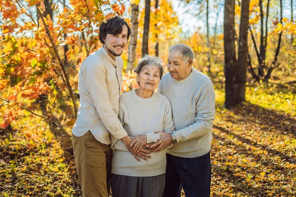 Nonna, nonno e nipote adulto che si abbracciano nel parco autunnale — Foto Stock