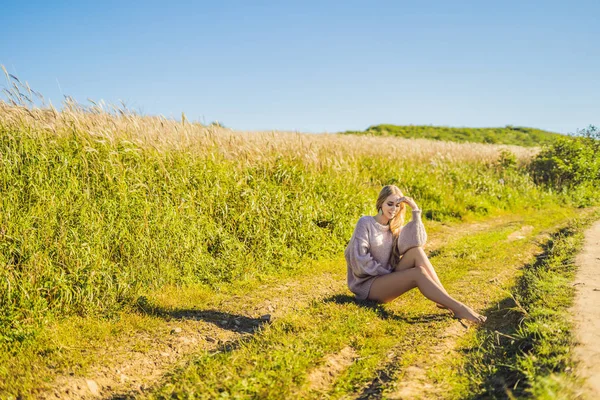 Giovane bella donna nel paesaggio autunnale con fiori secchi, spuntoni di grano. Moda autunno, inverno. Autunno soleggiato, maglione autunno accogliente. foto di moda — Foto Stock