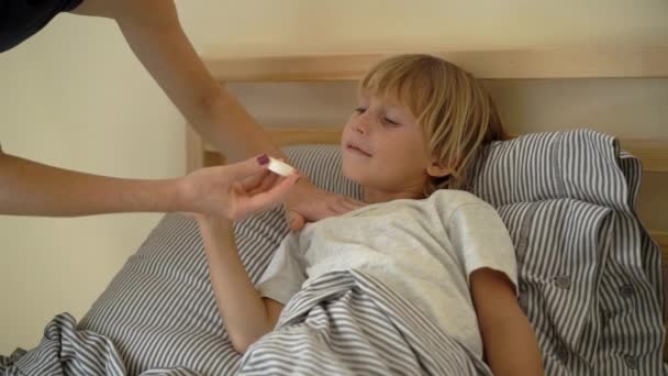 Tiro em câmara lenta de um rapazinho doente numa cama. Mãe esfrega meninos peito com pomada com óleos essenciais. Conceito de gripe infantil — Vídeo de Stock