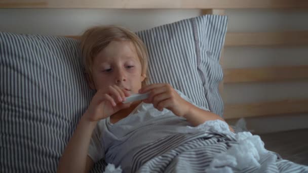 Um rapazinho a ver um termómetro e a ficar feliz com a sua temperatura. o conceito de recuperação da gripe — Vídeo de Stock