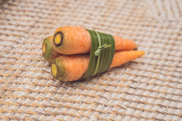 Eco-friendly product packaging concept. Carrot wrapped in a banana leaf, as an alternative to a plastic bag. Zero waste concept. Alternative packaging