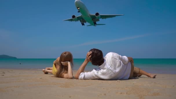 Superslowmotion shot of a happy man and woman tourists laying on a beautifull beach watching a landing airplane — Stock Video