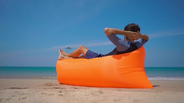Superslowmotion shot van gelukkige toerist leggen op een opblaasbare bank op een tropisch strand kijken naar een vliegtuig landing — Stockvideo