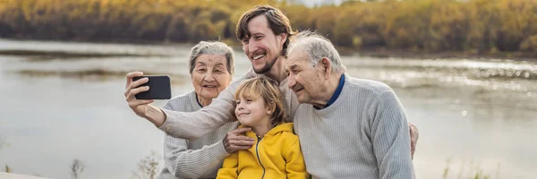 BANNER, FORMATO LARGO Pareja mayor con nieto y bisnieto tomar una selfie en el parque de otoño. Bisabuela, bisabuelo y bisnieto — Foto de Stock