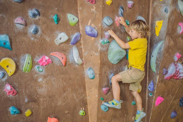 Little boy climbing a rock wall in special boots. indoor — Stock Photo, Image