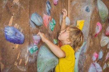 Küçük çocuk özel botlar içinde bir kaya duvarına tırmanıyor. Kapalı