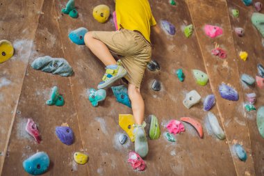 Küçük çocuk özel botlar içinde bir kaya duvarına tırmanıyor. Kapalı