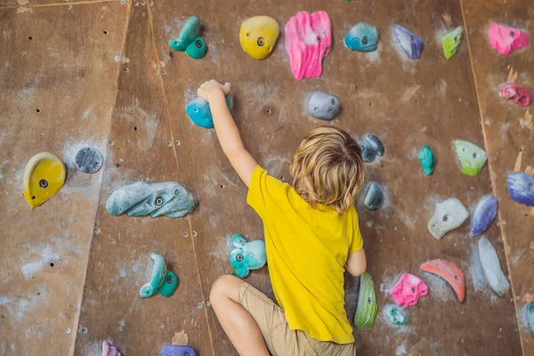 Little boy climbing a rock wall in special boots. indoor — Stock Photo, Image