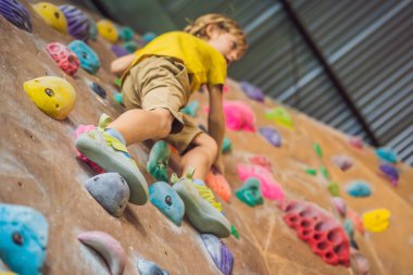 Küçük çocuk özel botlar içinde bir kaya duvarına tırmanıyor. Kapalı