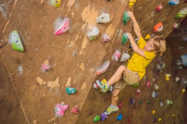 Küçük çocuk özel botlar içinde bir kaya duvarına tırmanıyor. Kapalı