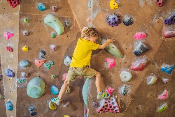 Kleiner Junge klettert in Spezialstiefeln eine Felswand hinauf. Innenräume — Stockfoto