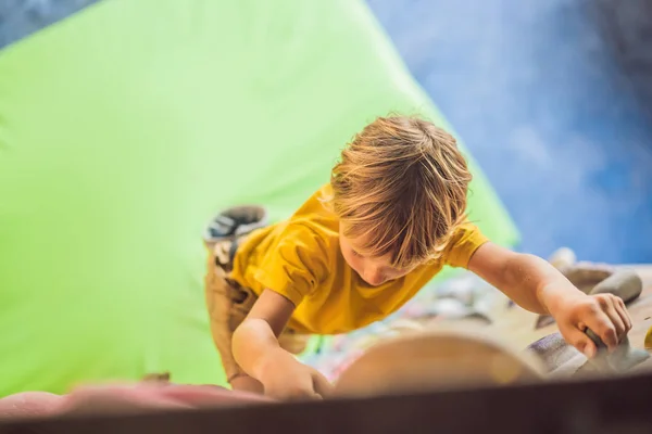 Kleiner Junge klettert in Spezialstiefeln eine Felswand hinauf. Innenräume — Stockfoto