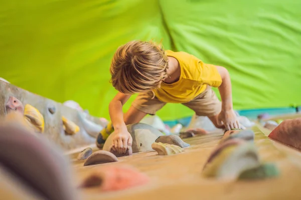 Little boy climbing a rock wall in special boots. indoor — Stock Photo, Image