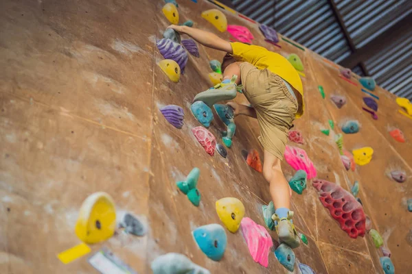 Little boy climbing a rock wall in special boots. indoor — Stock Photo, Image