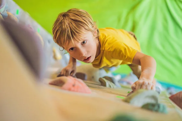 Kleiner Junge klettert in Spezialstiefeln eine Felswand hinauf. Innenräume — Stockfoto