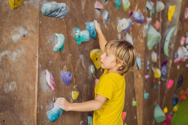 Pikkupoika kiipeää kallioseinälle erikoissaappaissa. sisätiloissa — kuvapankkivalokuva