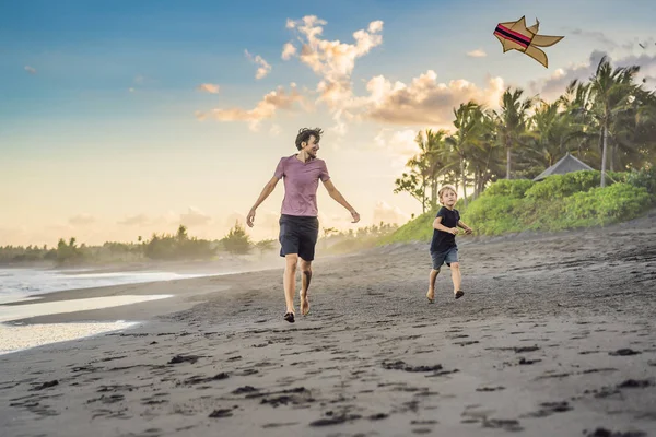 Молодой отец и его сын бегают с воздушным змеем на пляже — стоковое фото