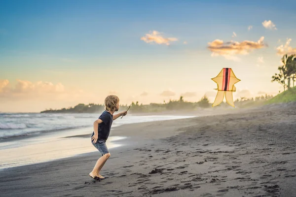 Felice giovane ragazzo aquilone volante sulla spiaggia al tramonto — Foto Stock