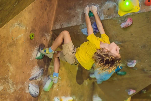 Küçük çocuk özel botlar içinde bir kaya duvarına tırmanıyor. Kapalı