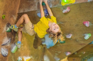 Küçük çocuk özel botlar içinde bir kaya duvarına tırmanıyor. Kapalı