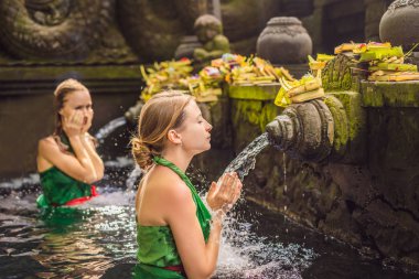 Two women in holy spring water temple in bali. The temple compound consists of a petirtaan or bathing structure, famous for its holy spring water clipart