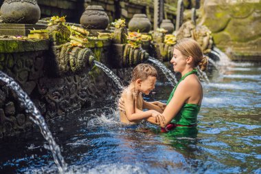 Mother and son in holy spring water temple in bali. The temple compound consists of a petirtaan or bathing structure, famous for its holy spring water clipart