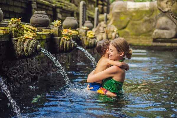 Madre e hijo en templo de agua de manantial santa en Bali. El complejo del templo consiste en un petirtaan o estructura de baño, famoso por su agua de manantial santa — Foto de Stock