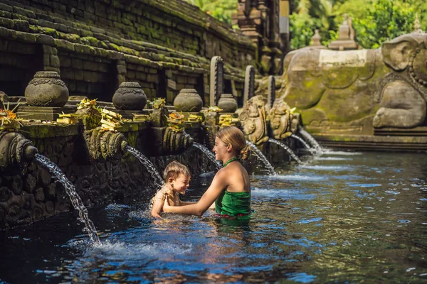 Madre e hijo en templo de agua de manantial santa en Bali. El complejo del templo consiste en un petirtaan o estructura de baño, famoso por su agua de manantial santa — Foto de Stock