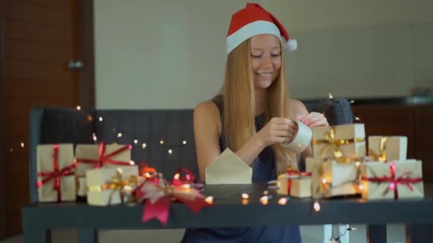 Die Zeitlupe einer jungen Frau packt Geschenke ein. Geschenk eingewickelt in Bastelpapier mit einem rot-goldenen Band für Weihnachten oder Neujahr. Frau bastelt Adventskalender für ihre Kinder