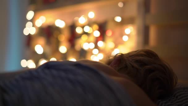 Slowmotion bir gelişme takvimi ile yatakta uyuyan küçük bir çocuk çekim Noel ışıkları ile hafifletmek onun yatağın bir arka parlar. Noel ve yeni yıl konsepti için hazırlanıyor. Advent takvimi — Stok video