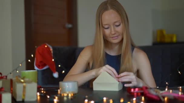 Die Zeitlupe einer jungen Frau packt Geschenke ein. Geschenk eingewickelt in Bastelpapier mit einem rot-goldenen Band für Weihnachten oder Neujahr. Frau bastelt Adventskalender für ihre Kinder