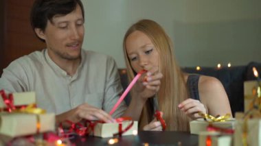 Genç bir kadın ve adam baba ve anne Wrap Slowmotion çekim hediyeler. Presents Noel veya yeni yıl için kırmızı ve altın kurdele ile Craft kağıt sarılmış. Ebeveynler için bir geliş takvimi yapmak