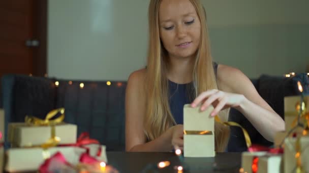 La toma en cámara lenta de una mujer joven está empacando regalos. Presente envuelto en papel artesanal con una cinta roja y dorada para Navidad o año nuevo. Mujer hace un calendario de adviento para sus hijos — Vídeo de stock