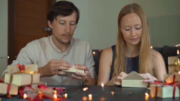 Slowmotion shot van een jonge vrouw en man vader en moeder wrap presenteert. Presenteert verpakt in ambachtelijke papier met een rood en goud lint voor Kerstmis of Nieuwjaar. Ouders maken een adventskalender voor — Stockvideo