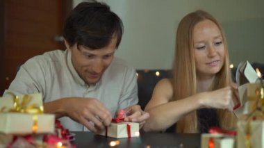 Genç bir kadın ve adam baba ve anne Wrap Slowmotion çekim hediyeler. Presents Noel veya yeni yıl için kırmızı ve altın kurdele ile Craft kağıt sarılmış. Ebeveynler için bir geliş takvimi yapmak
