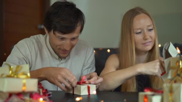 Slowmotion shot of a young woman and man father and mother wrap presents. Presents wrapped in craft paper with a red and gold ribbon for Christmas or new year. Parents make an advent calendar for — Stock Video